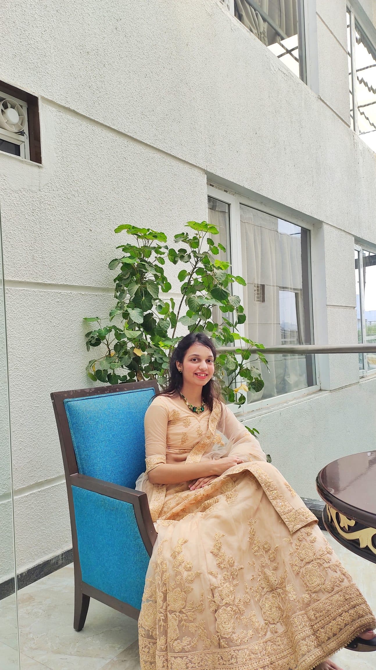 Ruchika Jharbade seated in a peach and gold embroidered anarkali with an emerald necklace, smiling.